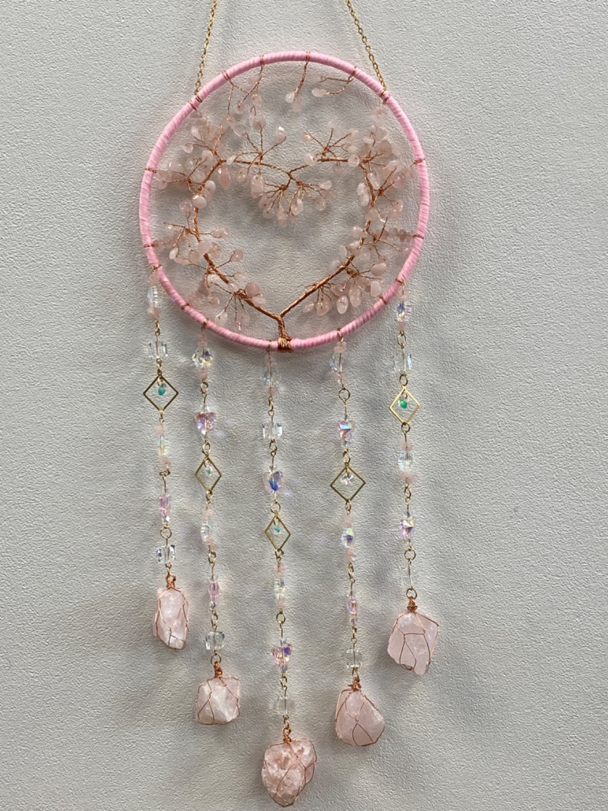 Pink-wrapped circular tree of life hanger with dried branches and raw rose quartz stones hanging from chains below