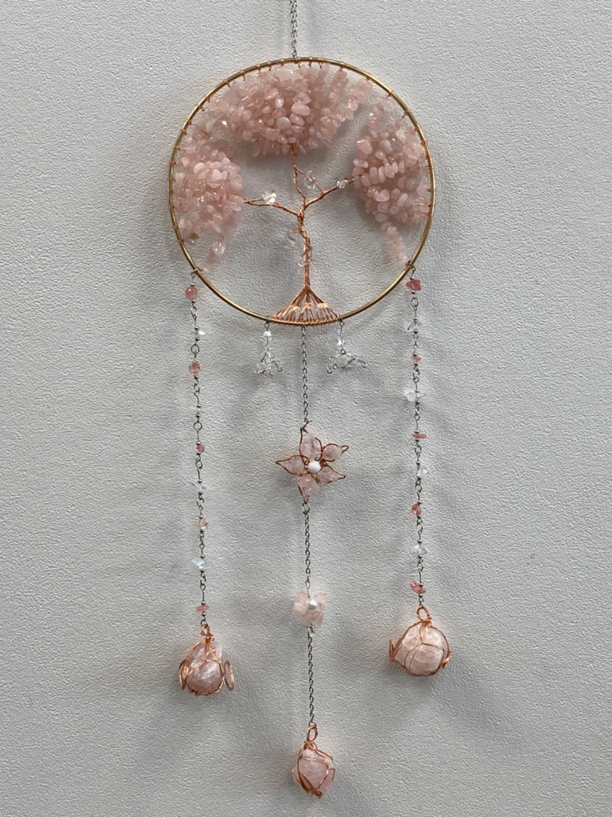 Rose quartz chip tree of life wall hanging with copper wire, featuring a circular frame, dangling chains, and rose quartz pendants.