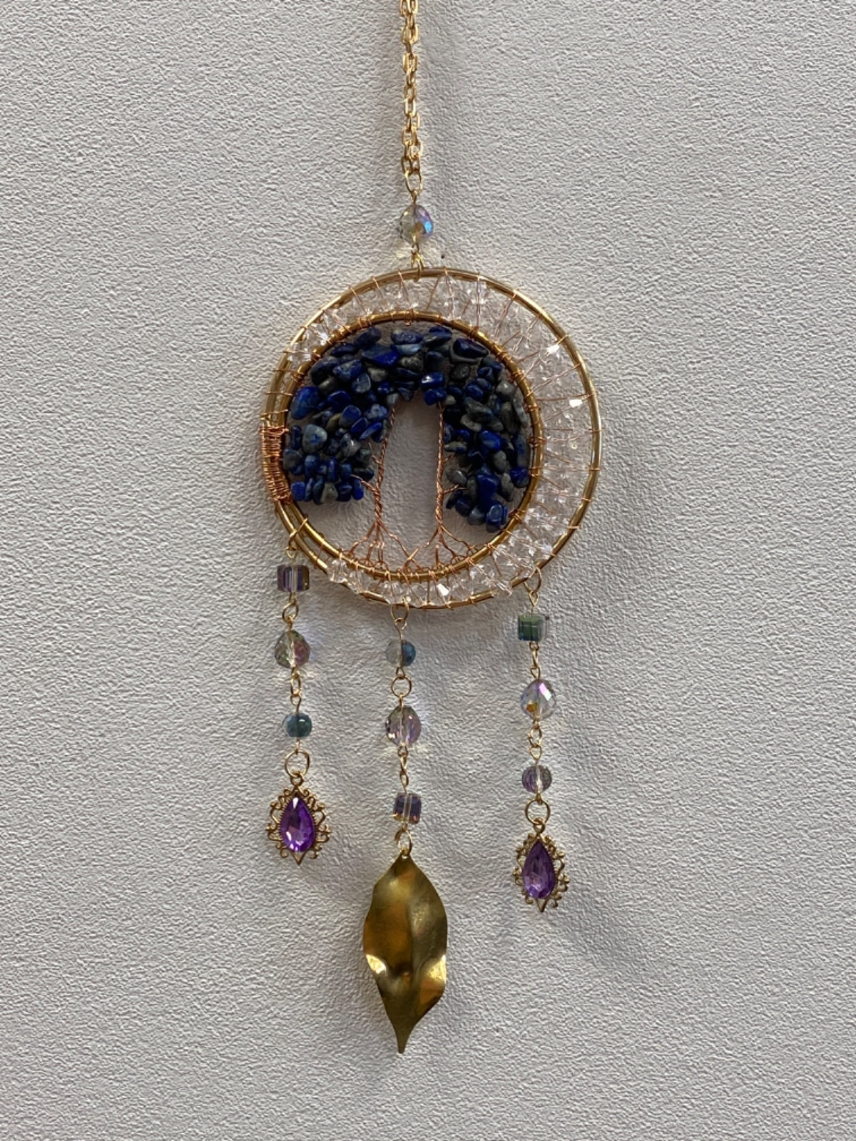 Circular wire tree of life pendant with lapis lazuli chips, crackle quartz ring, and three dangling brass and amethyst charms on a gold chain.