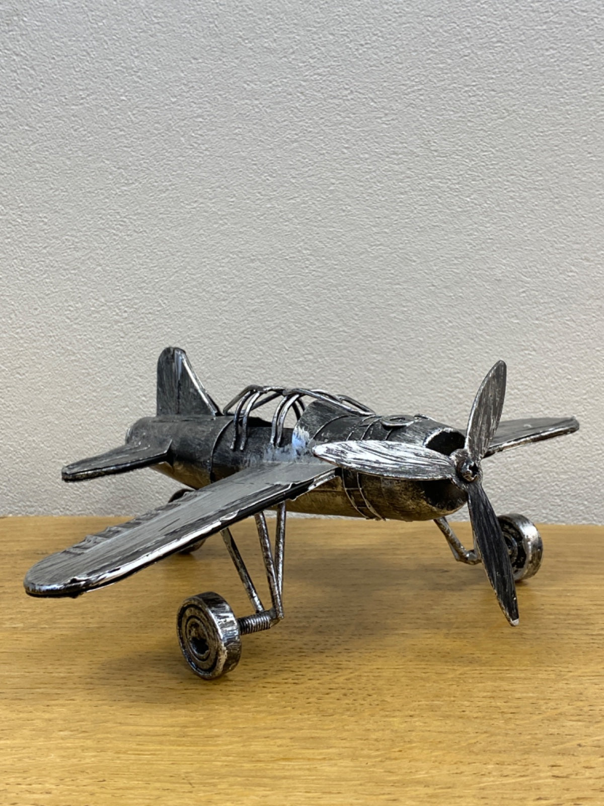 Handcrafted metal fighter plane model on wooden base, dark patina finish with bright propellers