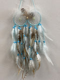 Blue and brown feather dream catcher with turquoise web, beaded strands, and natural feathers hanging against white wall.