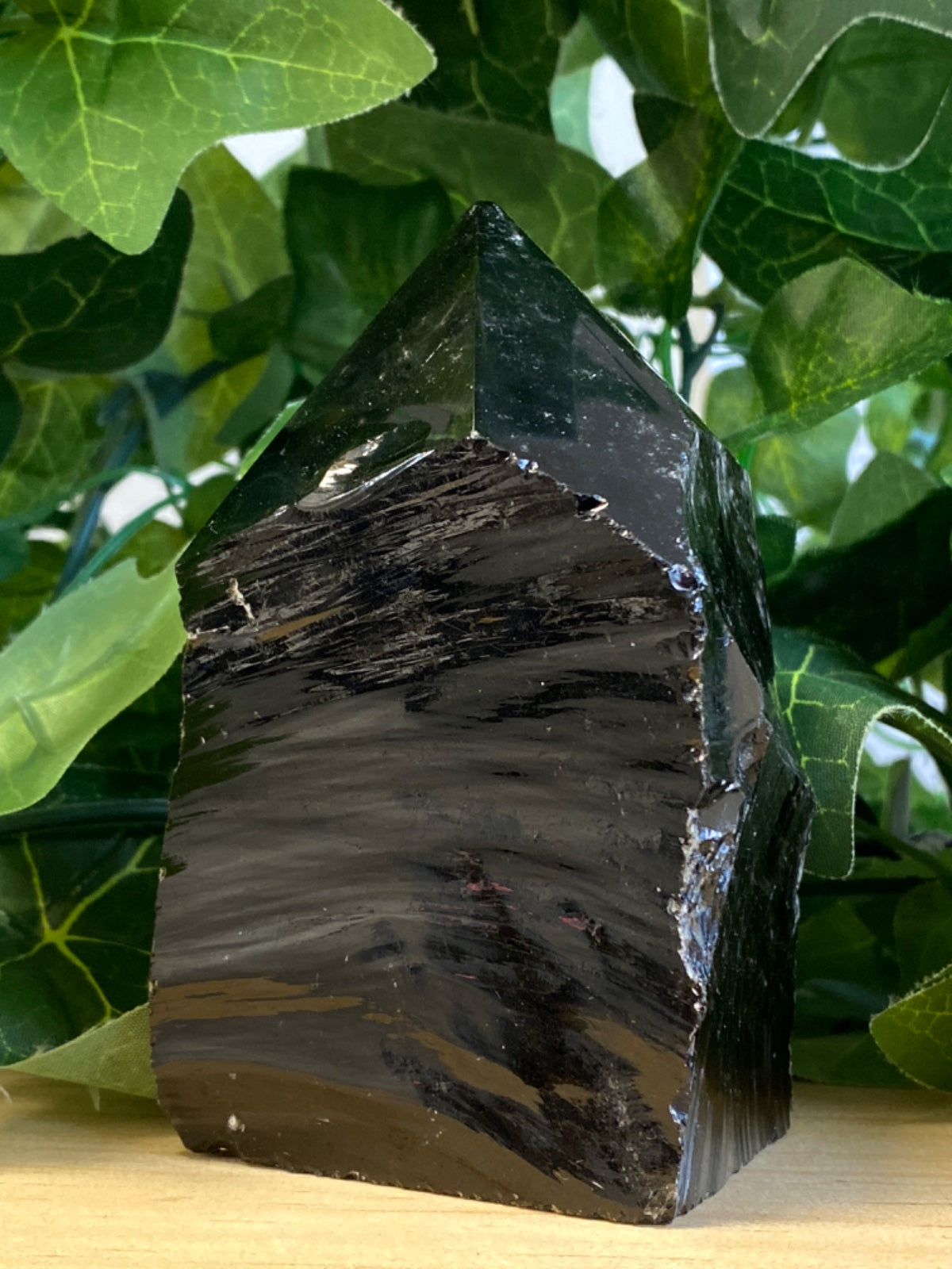 Raw obsidian point, 470g, polished black stone with layered banding, displayed among green foliage
