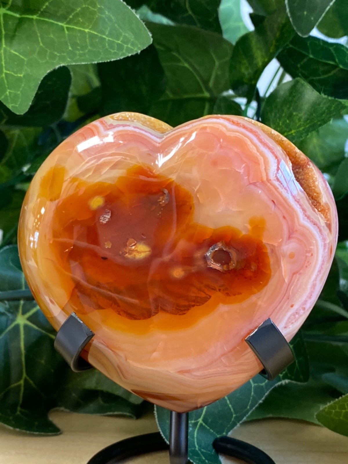 Polished carnelian heart with raw geode cavity, peachy-orange tones, displayed on black stand