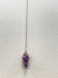 Amethyst pendulum with silver spiral wire wrap hanging from a delicate chain against a white wall