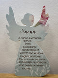 White angel figurine plaque with printed text about nannies and a pink flower tucked into the right wing