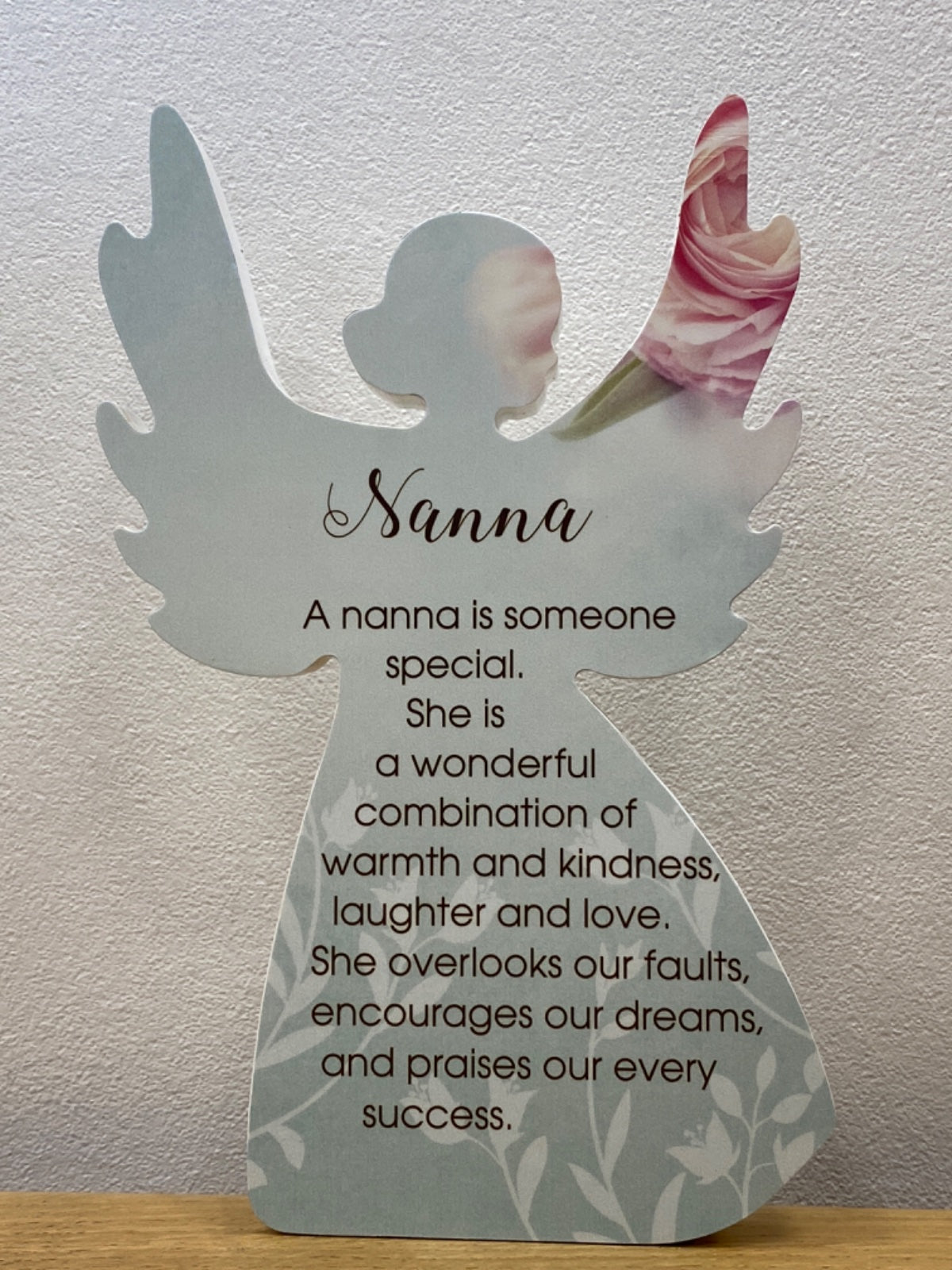 White angel figurine plaque with printed text about nannies and a pink flower tucked into the right wing