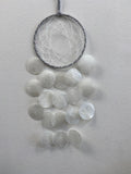 White dreamcatcher with grey-wrapped ring and delicate web, hanging above a cascade of translucent white shell discs
