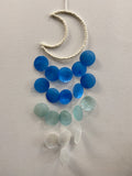 Blue dream catcher wind chimes with blue and pale green resin beads on cream rope against white wall
