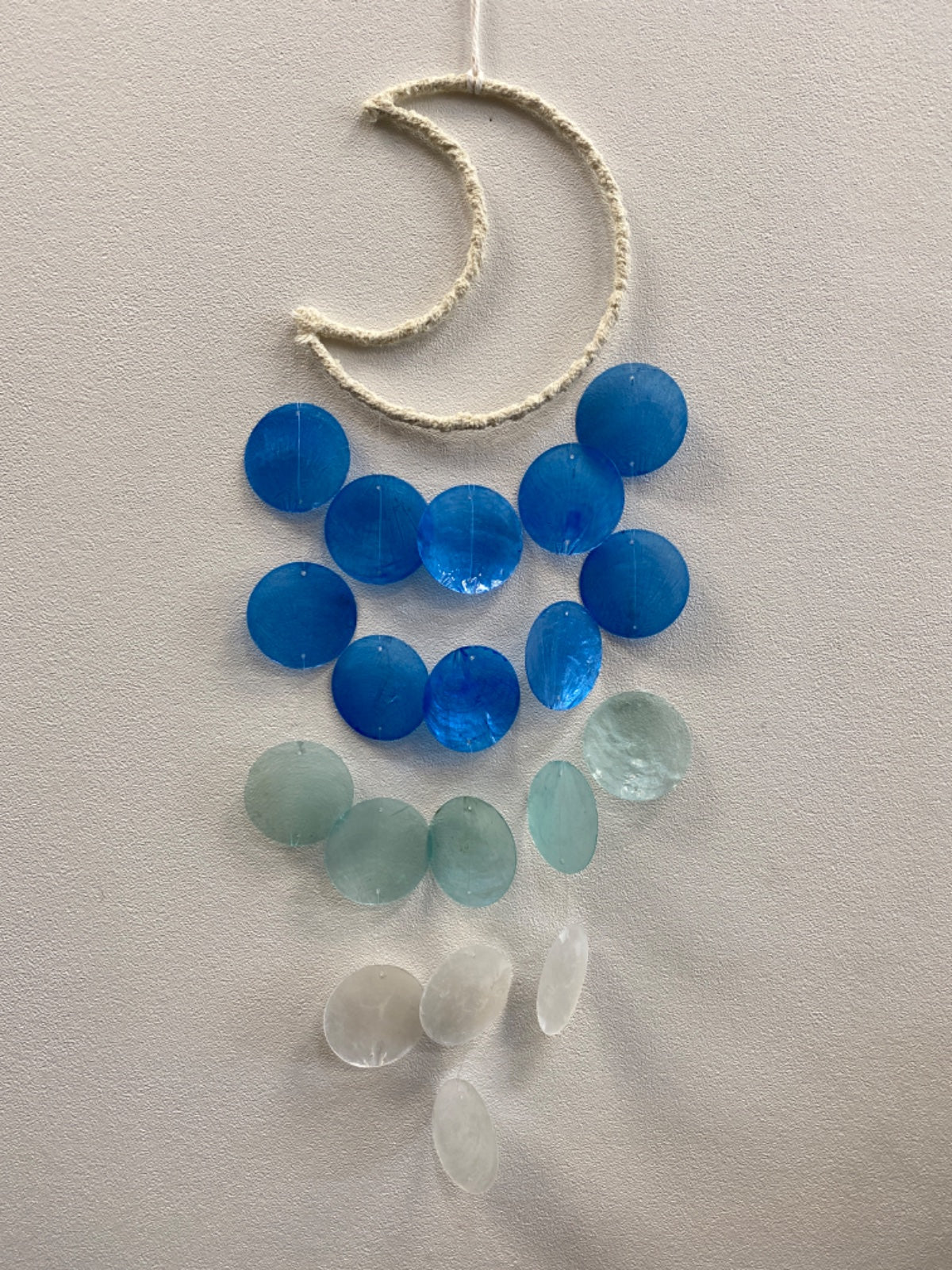 Blue dream catcher wind chimes with blue and pale green resin beads on cream rope against white wall