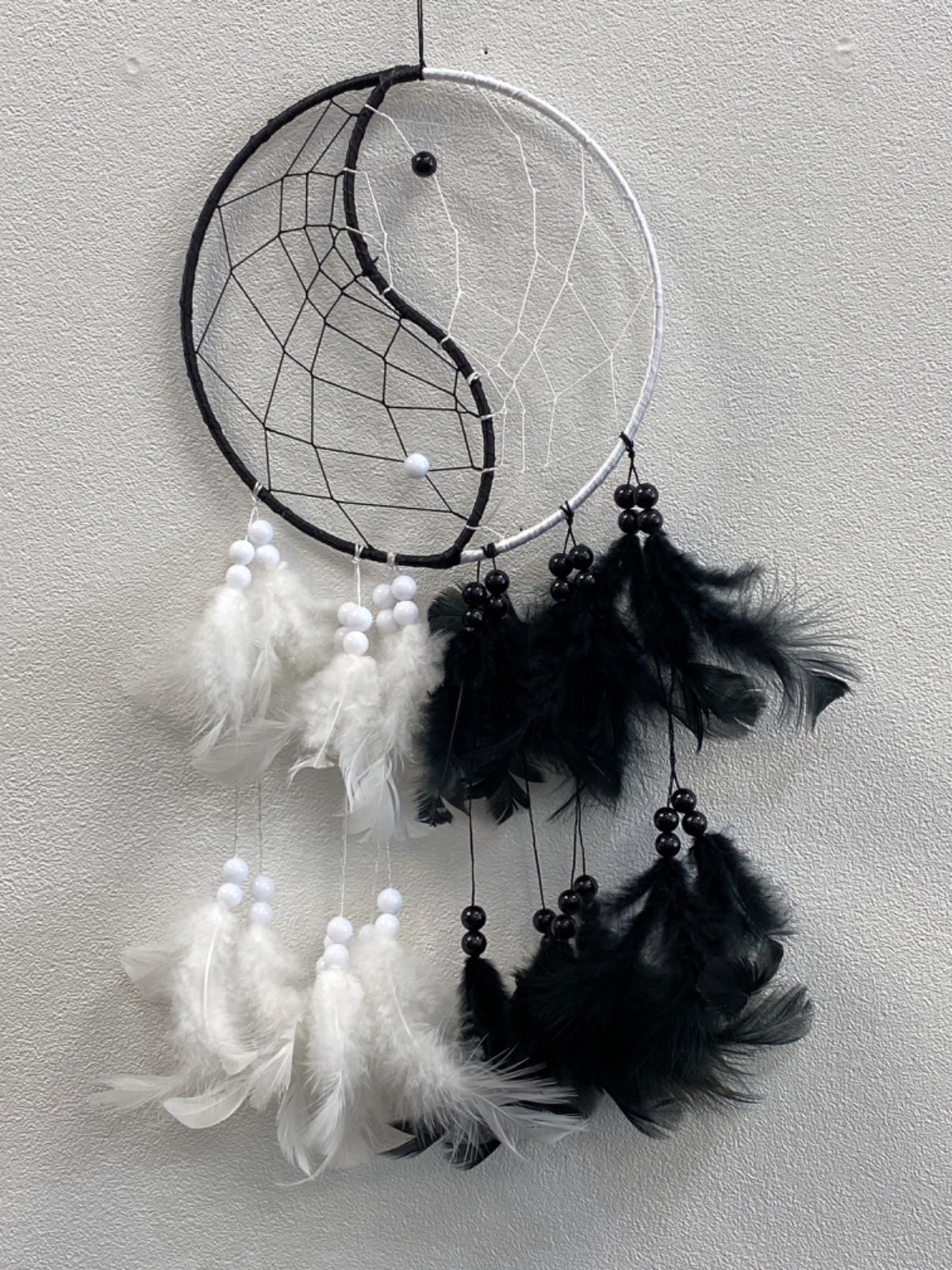 Black and white yin-yang dreamcatcher with woven web, black and white feathers, and black beads hanging from the ring.