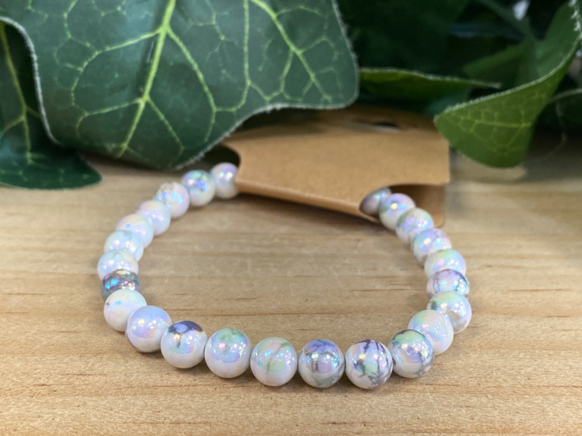 White howlite beaded bracelet with iridescent coating, 8mm beads, displayed on natural wood with green plant leaves.