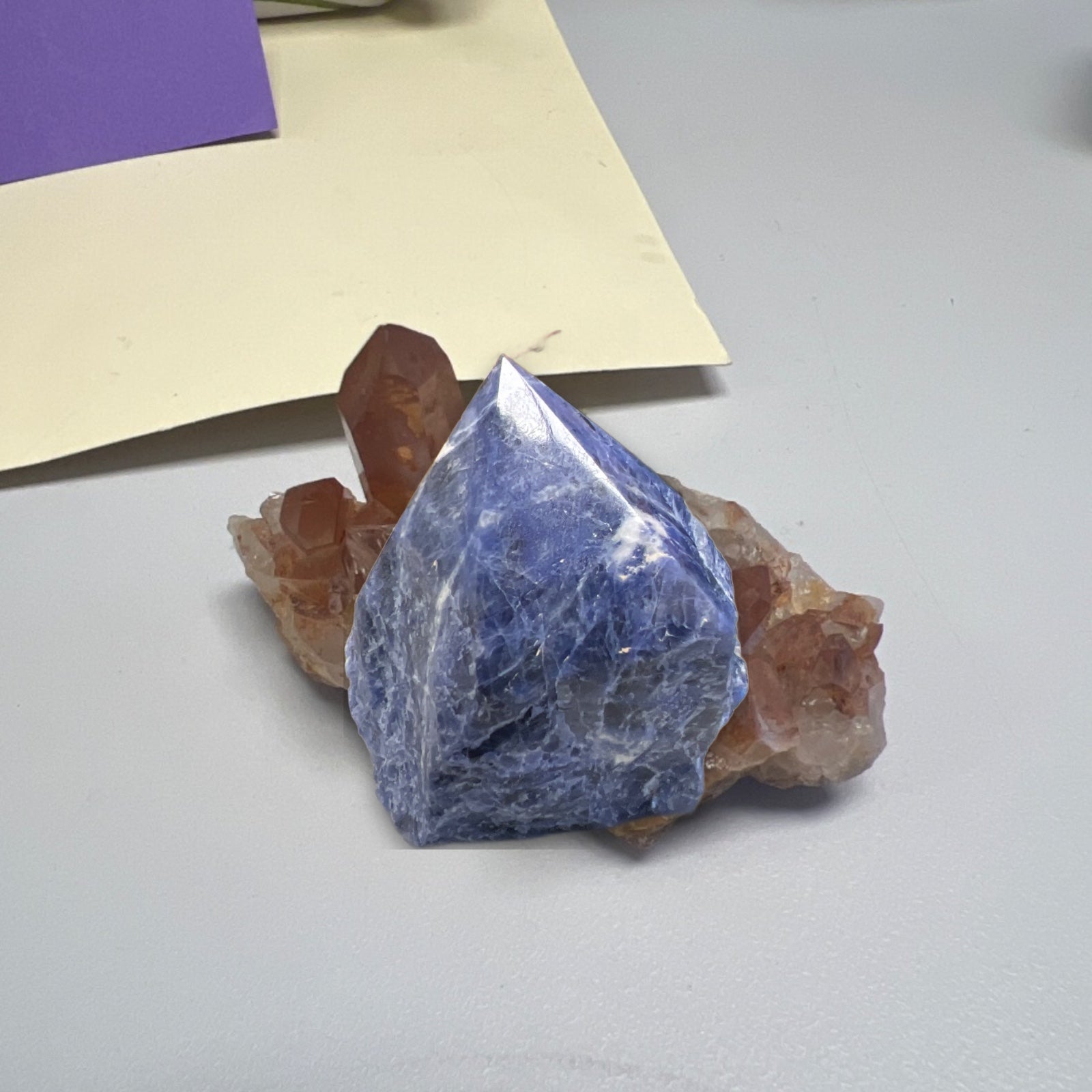 Raw sodalite chunk with deep blue coloring on tan matrix, displayed against cream paper