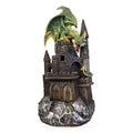 Green and gold dragon perched on dark stone castle tower with glowing red mouth, rocky base