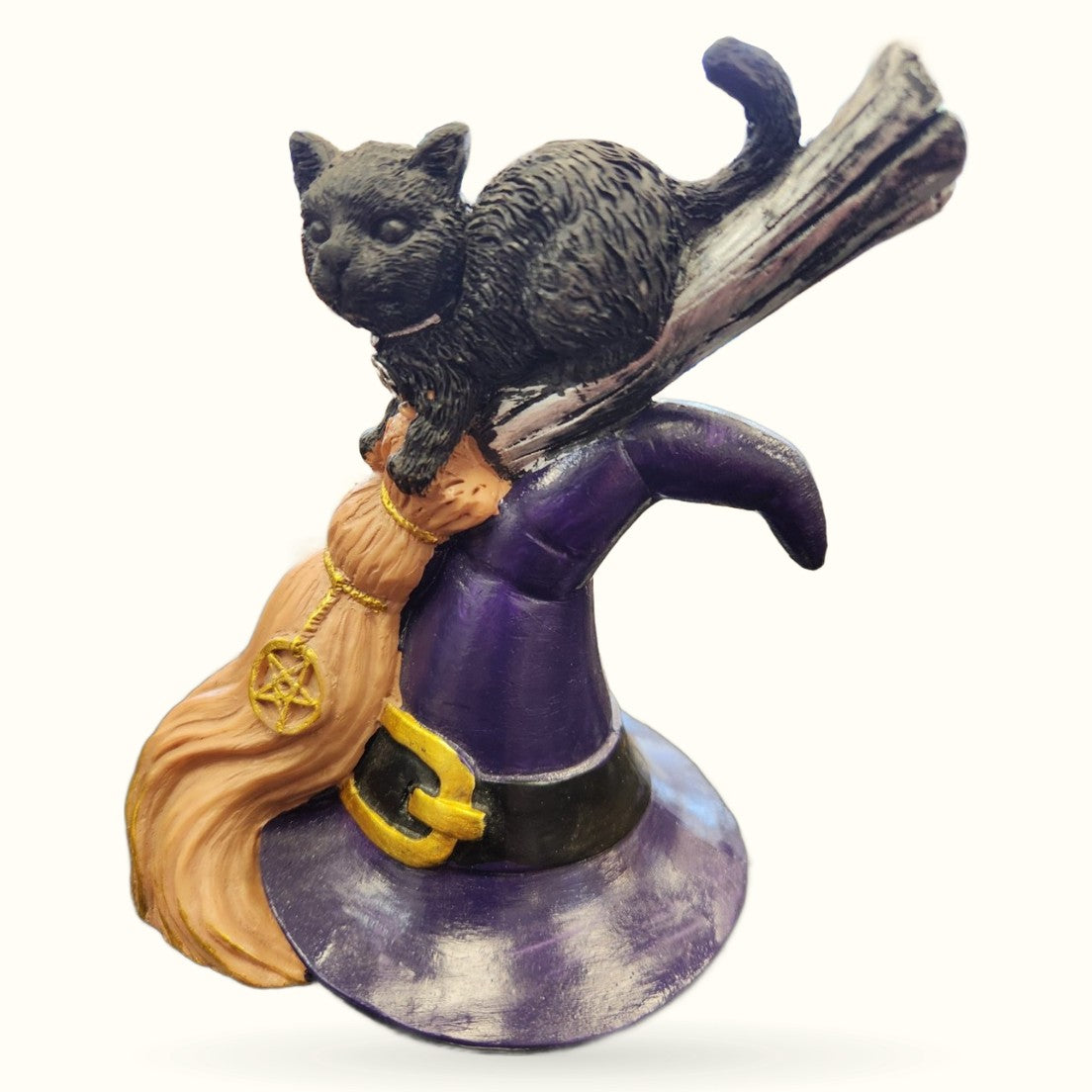 Black cat figurine perched on wooden broomstick wearing purple witch's hat and tan cloak with gold pentagram