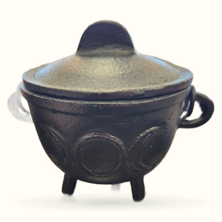 Black cast iron cauldron with lid, three legs, decorative circular motifs, and side handles