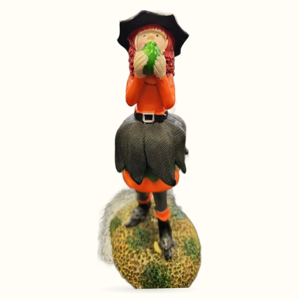 Whimsical witch figurine with red hair and black hat kissing a green frog, standing on a moss-covered rock