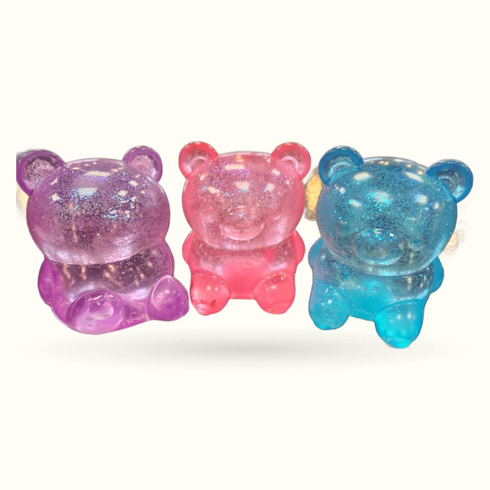 Three translucent bear-shaped toys in purple, pink, and blue with glitter sparkle finish