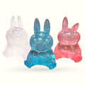 Three glowing rabbit figurines in translucent pastel colours: lavender, turquoise, and pink, each with sparkly details