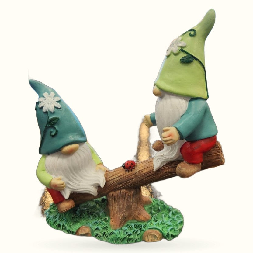 Two colorful garden gnomes on a wooden see-saw with green grass base