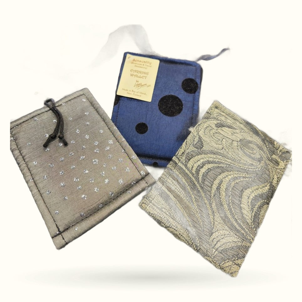 Three fabric earring wallets in navy with polka dots, gray with silver sparkles, and cream with geometric pattern
