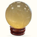 Polished citrine sphere on wooden stand, pale yellow translucent crystal with glossy finish