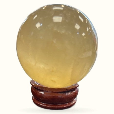 Polished citrine sphere on wooden stand, pale yellow translucent crystal with glossy finish