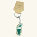 Green agate slice keychain with silver chain and ring, attached to EarthInspired packaging tag