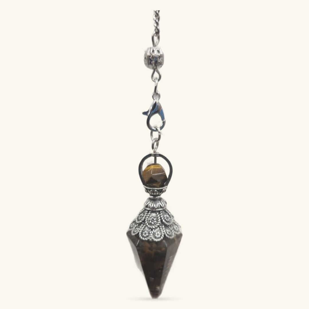 Tigers Eye crystal pendulum with ornate silver metalwork cap and filigree details, hanging from delicate chain