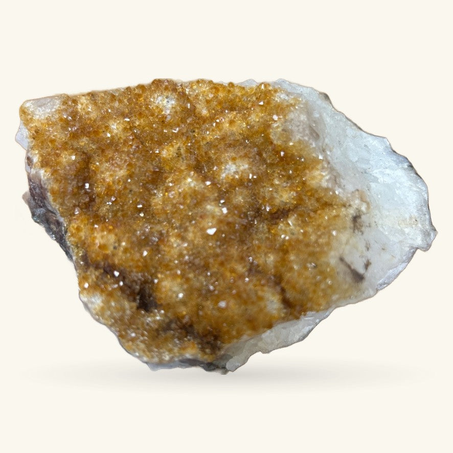 Raw citrine cluster with golden-brown crystals and white matrix on cream background