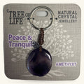 Purple amethyst sphere keychain with tree of life charm on beaded cord, displayed on branded packaging