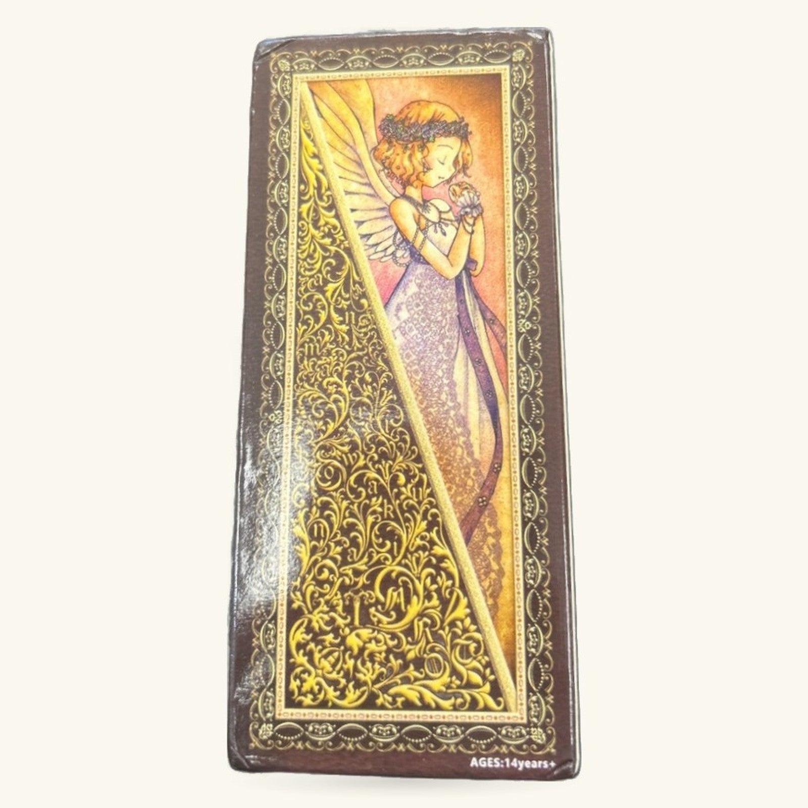 Slim tarot card deck with ornate gold filigree border and illustration of winged fairy figure in purple and pink robes