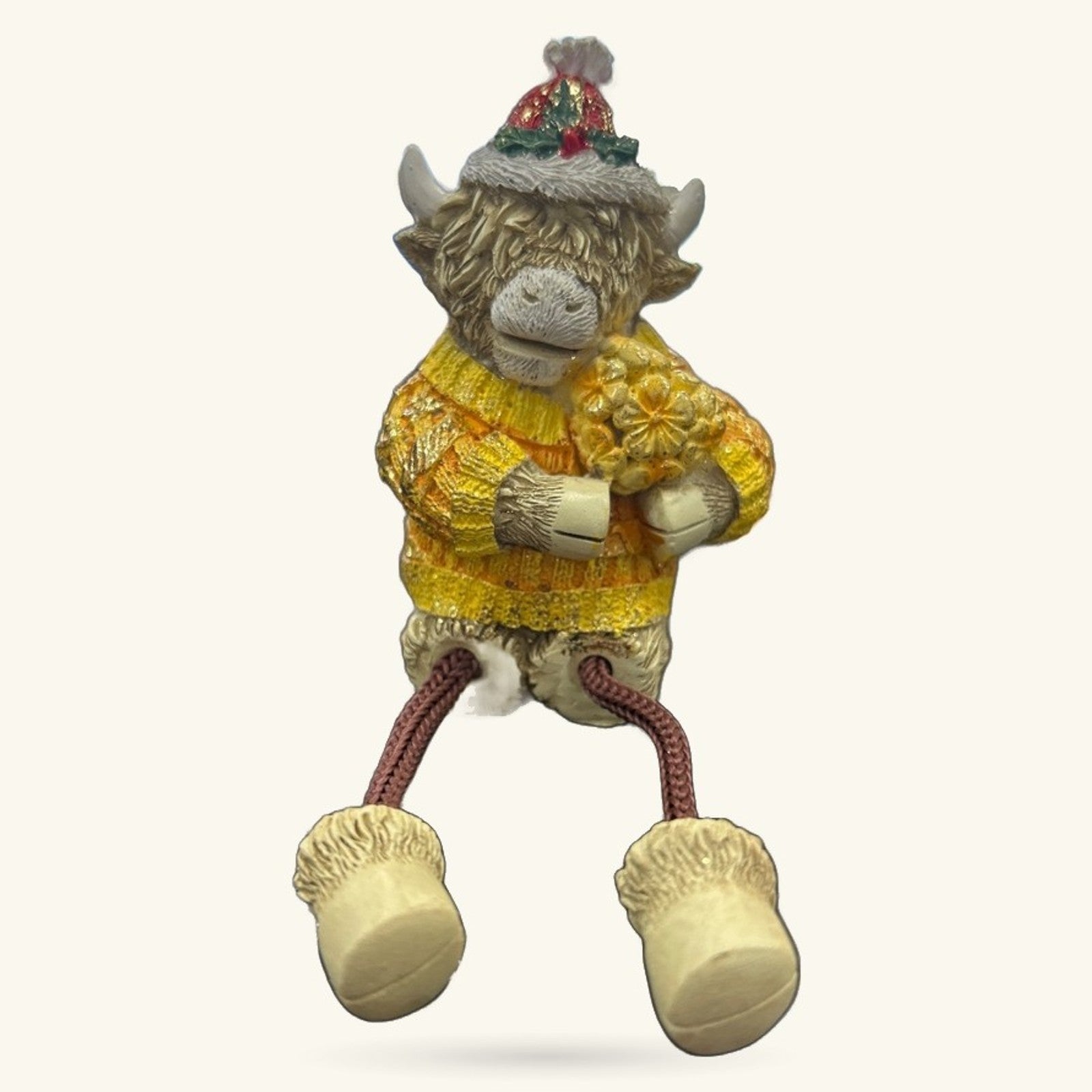 Ceramic Highland cow figurine wearing yellow sweater and festive hat with dangly rope legs