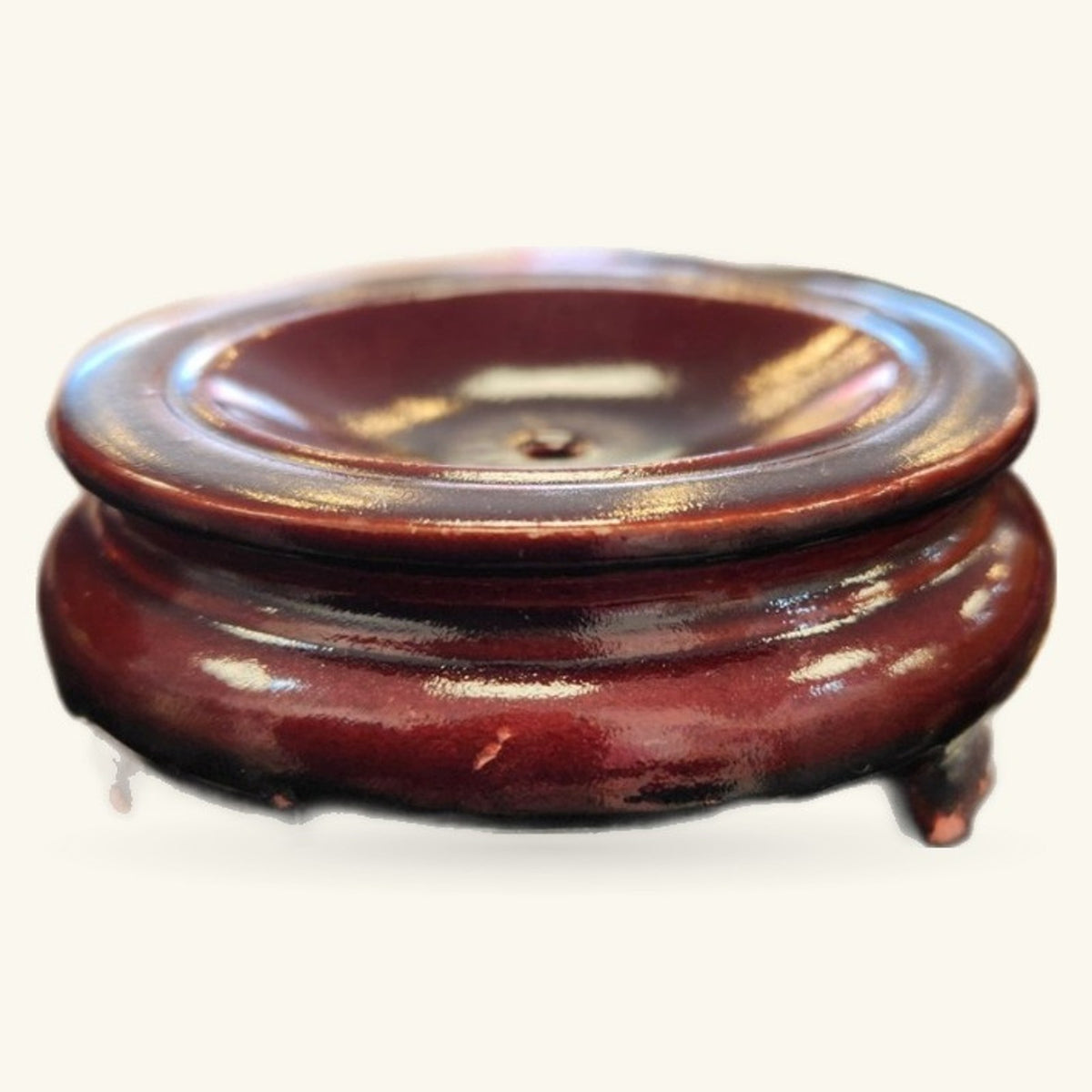 Burgundy wooden stand with three short legs, featuring a circular inset for displaying crystal spheres