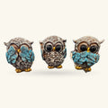 Three decorative owl figurines in see-hear-speak no evil poses with turquoise wings and gold feet
