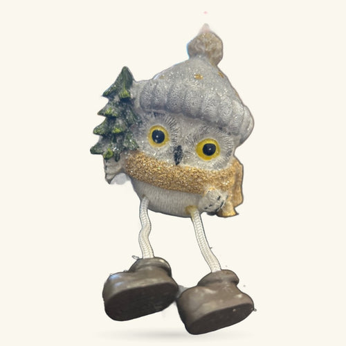 Grey ceramic Christmas owl ornament with golden glitter chest, yellow eyes, dangling brown legs, and small evergreen tree detail
