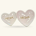 Two pale pink heart-shaped ceramic trinket trays with 'DREAM' written in gold script on each
