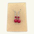 Pair of red bead earrings on a kraft paper display card with silver-toned hooks