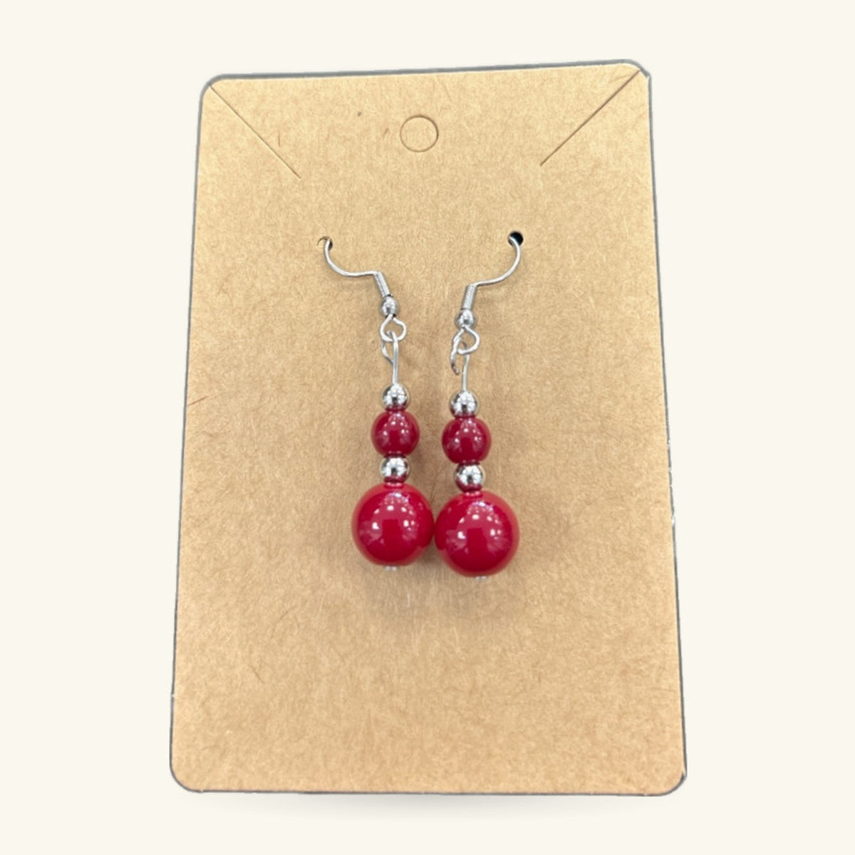 Pair of red bead earrings on a kraft paper display card with silver-toned hooks