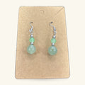 Pair of green jade bead earrings on a kraft paper display card with silver-toned hooks and spacer beads