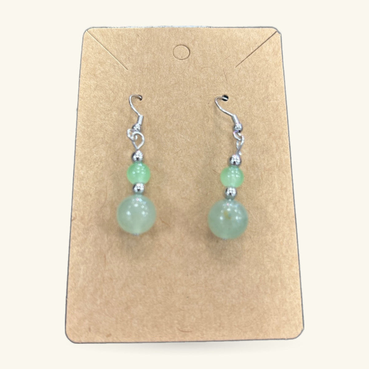 Pair of green jade bead earrings on a kraft paper display card with silver-toned hooks and spacer beads