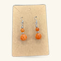Pair of orange bead earrings on kraft card display. Two-tier design with smaller and larger spheres.
