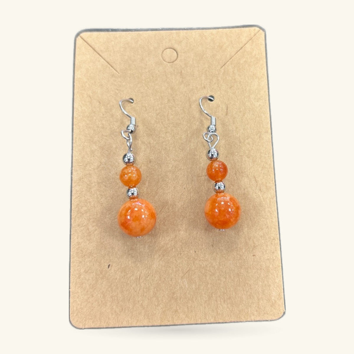 Pair of orange bead earrings on kraft card display. Two-tier design with smaller and larger spheres.