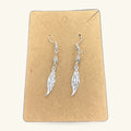 Pair of silver leaf-shaped dangle earrings on a kraft paper display card with fish hook wires