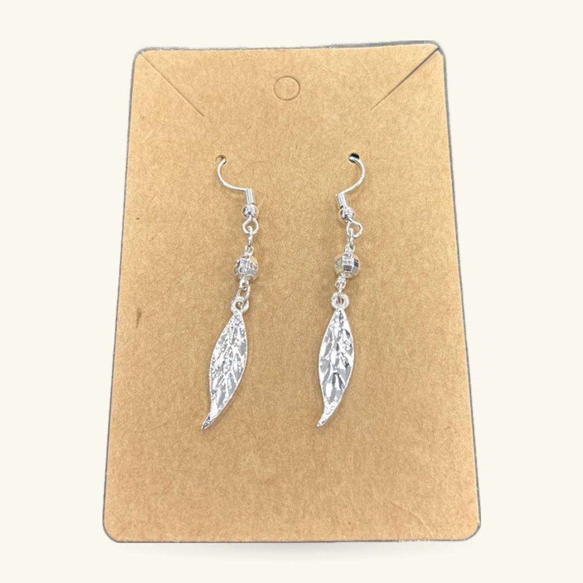 Pair of silver leaf-shaped dangle earrings on a kraft paper display card with fish hook wires
