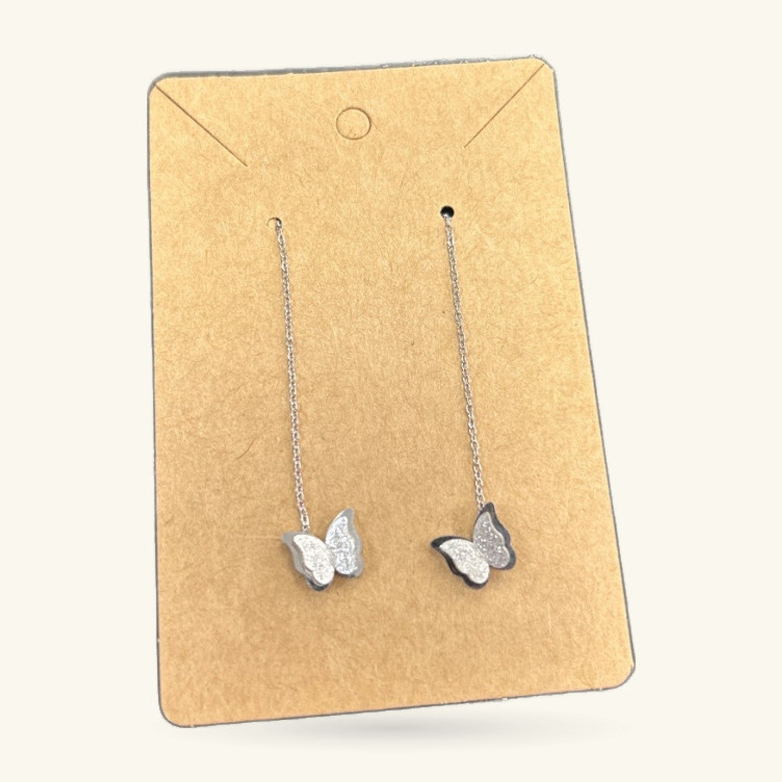 Pair of stainless steel butterfly earrings on chain hooks, displayed on kraft paper card