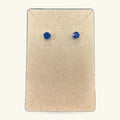 Pair of blue round stud earrings on a cream earring card with envelope flap