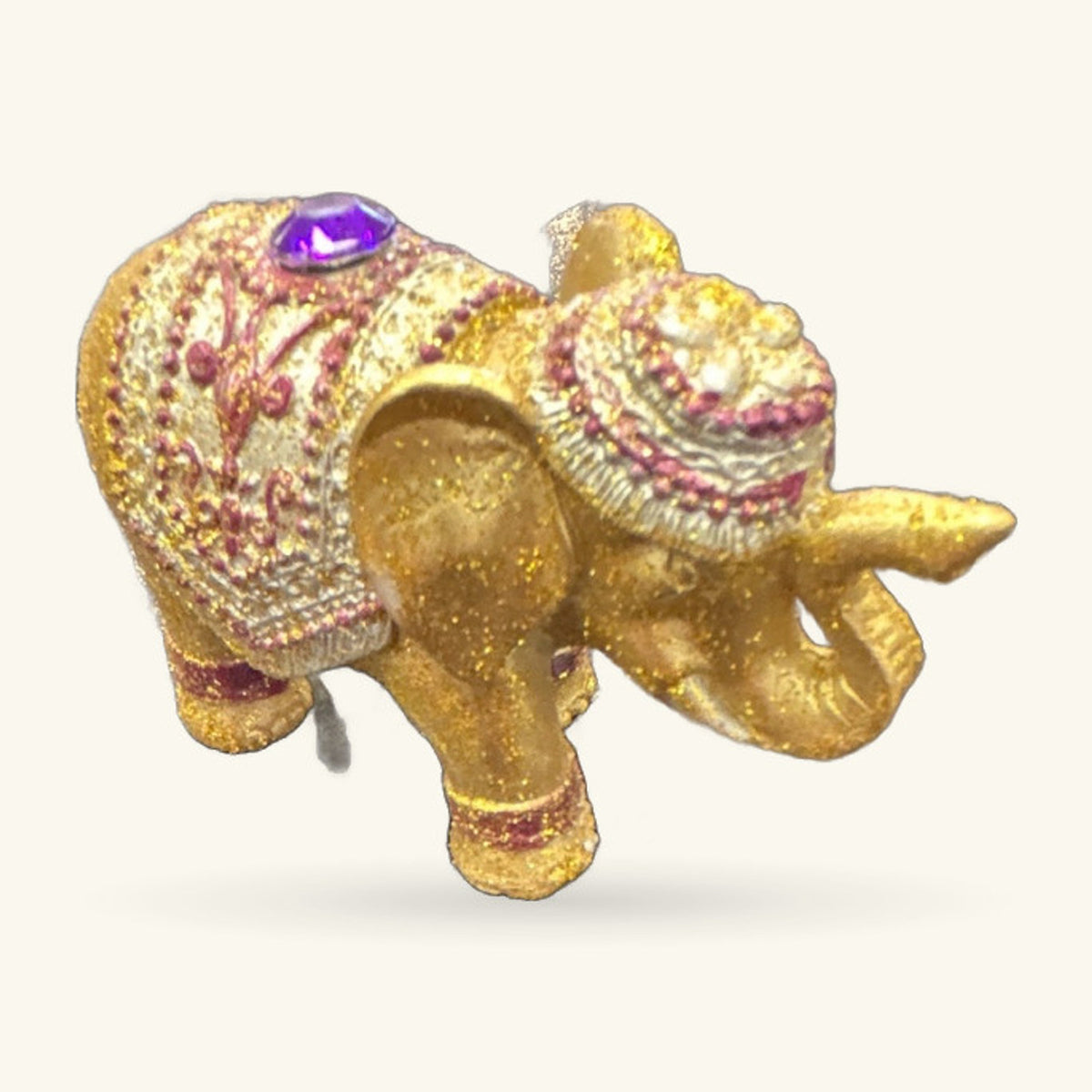 Gold glitter elephant figurine with purple gem on head, decorative incense holder with patterned blanket detail