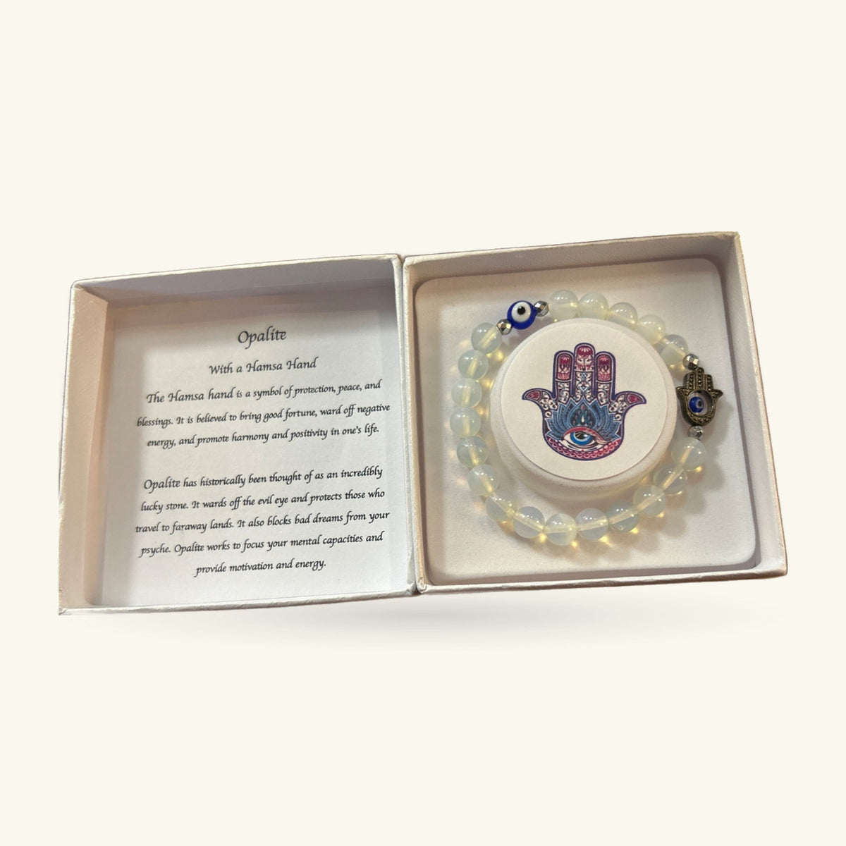 Opalite bead bracelet with hamsa hand pendant and evil eye charm, displayed in an open gift box with information card