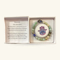 Amazonite bead bracelet with Hamsa hand charm and evil eye bead in open gift box, beside information card