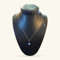 Evil eye necklace with small blue and white pendant on silver chain, displayed on black bust